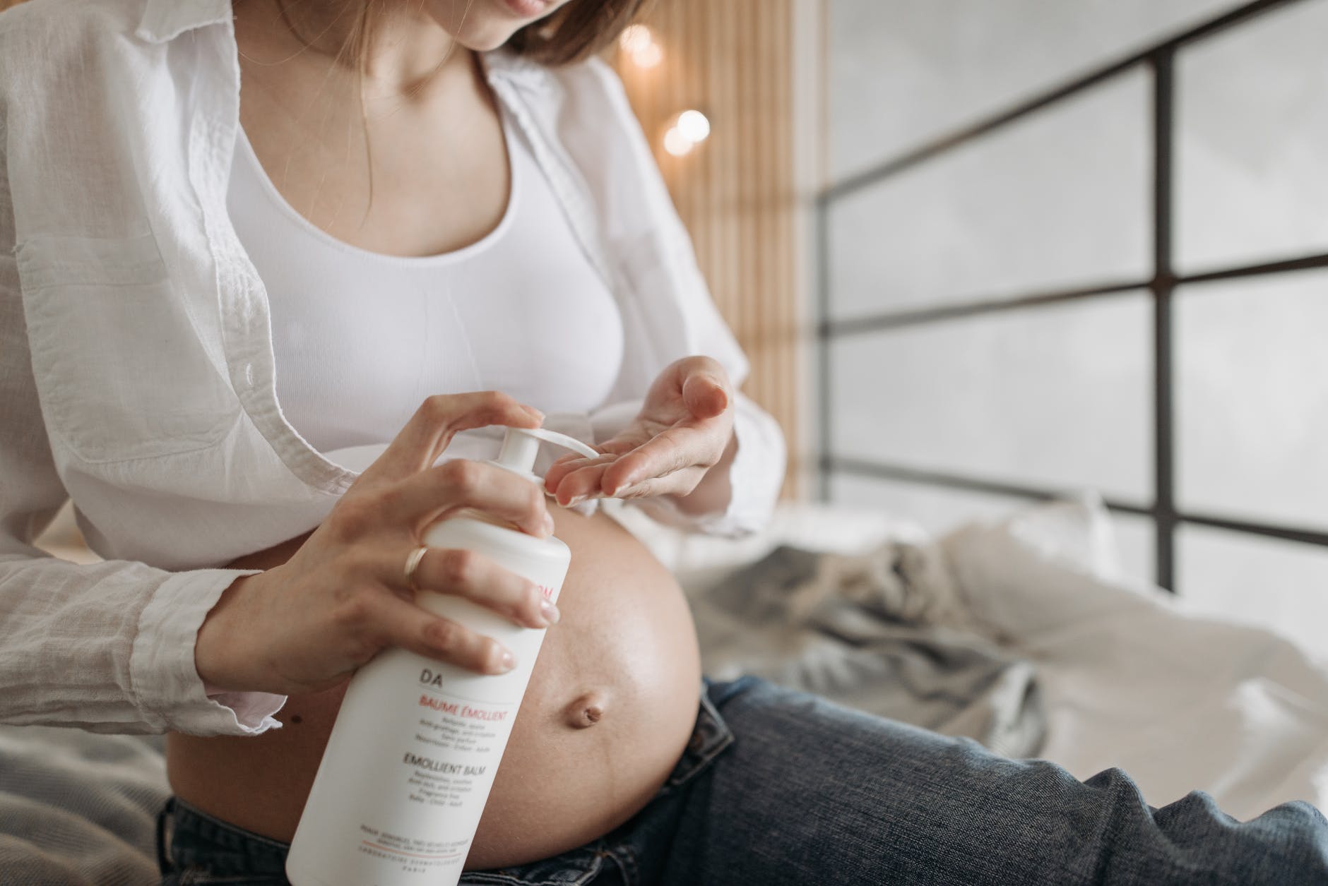 hands of a pregnant woman pumping lotion from a white bottle